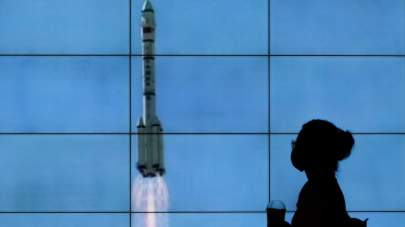 A woman wearing a face mask is silhouetted as she walks by a TV screen showing CCTV live telecast of the Long March-2F Y12 rocket carrying a crew of Chinese astronauts in a Shenzhou-12 spaceship lifts off at the Jiuquan Satellite Launch Center, at a shopping mall in Beijing, Thursday, June 17, 2021. China launched the first three crew members on a mission to its new space station Thursday in its first crewed mission in five years. (AP Photo/Andy Wong)